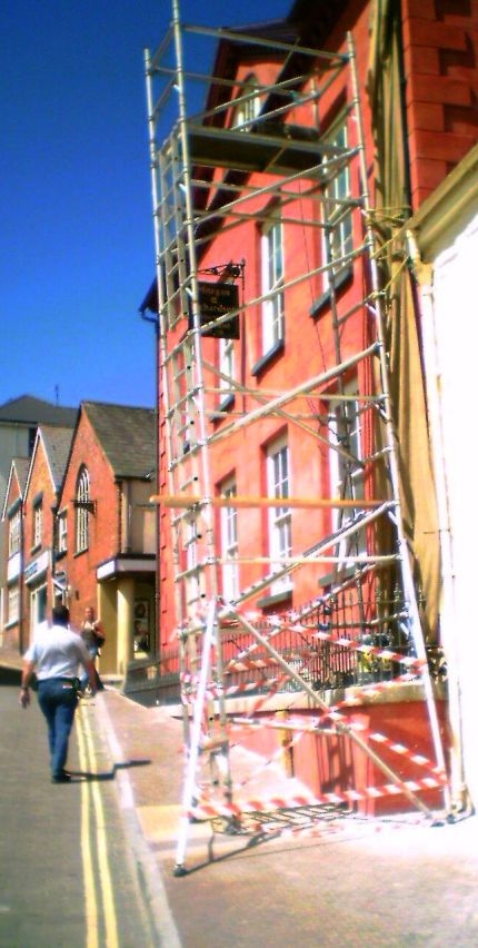 Badly-assembled mobile scaffold tower with insufficient gaurd rails, insufficient outrigger bracing, platform wrong way round, diagonal bracing incorrectly installed and leaning